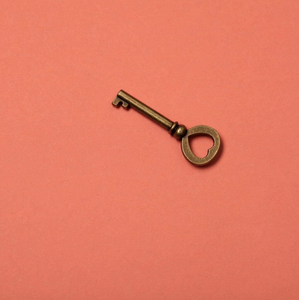 A vintage bronze key with a heart-shaped bow lies on a coral background.