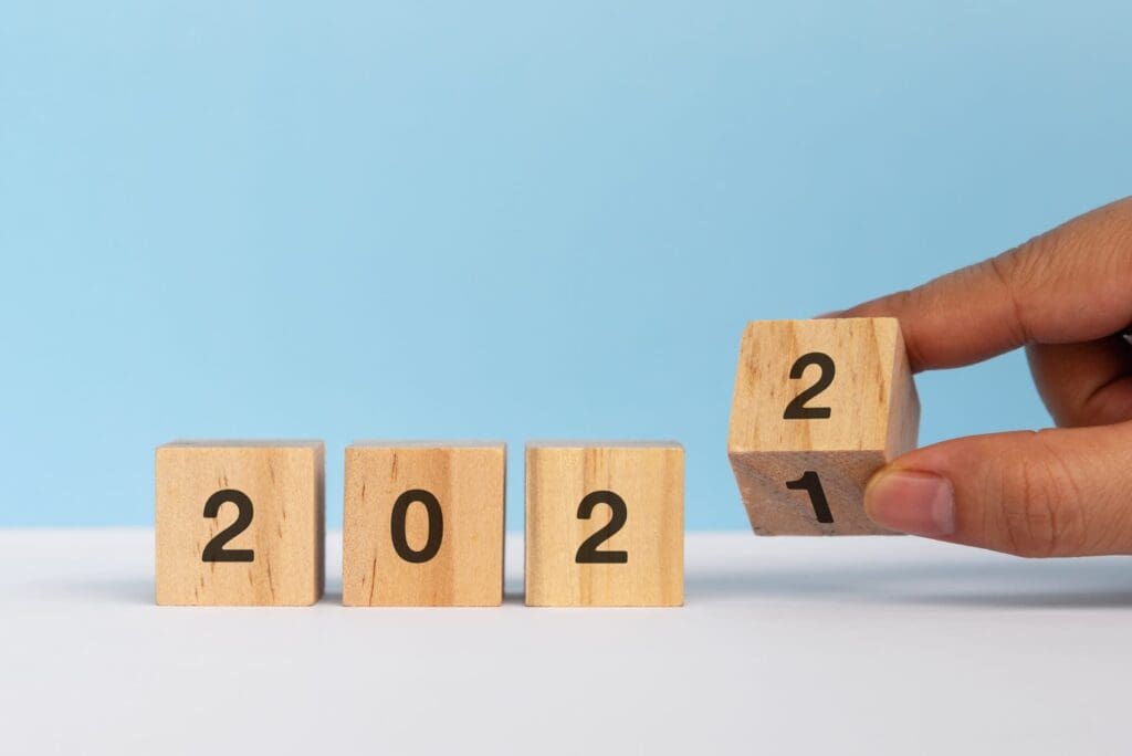 Wooden blocks display "2021" with a hand turning the last block to reveal "2022" against a blue background.