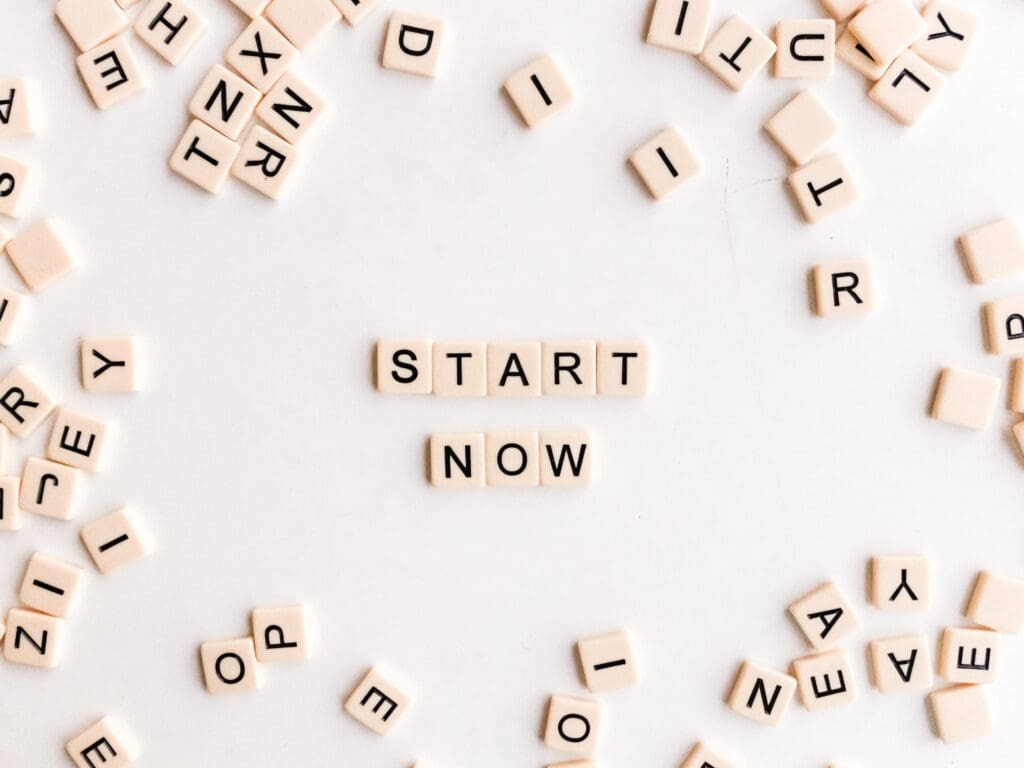 Scattered Scrabble tiles form the words "START NOW" in the center on a white background.